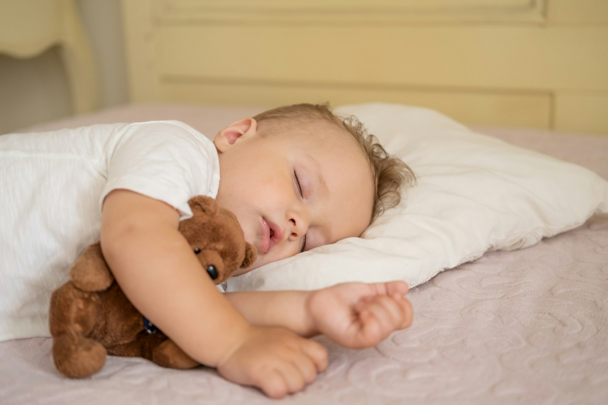 funny baby boy sleeping on bed at home. child hugging teddy bear